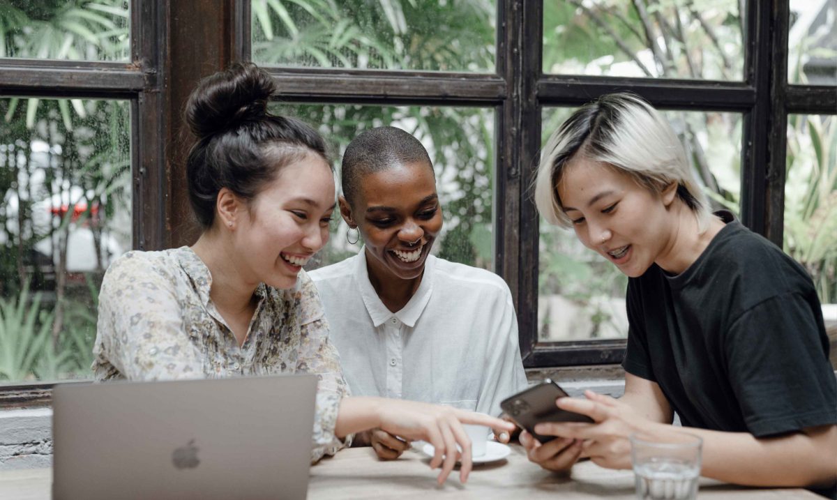 three young women laughing and pointing at phone screen